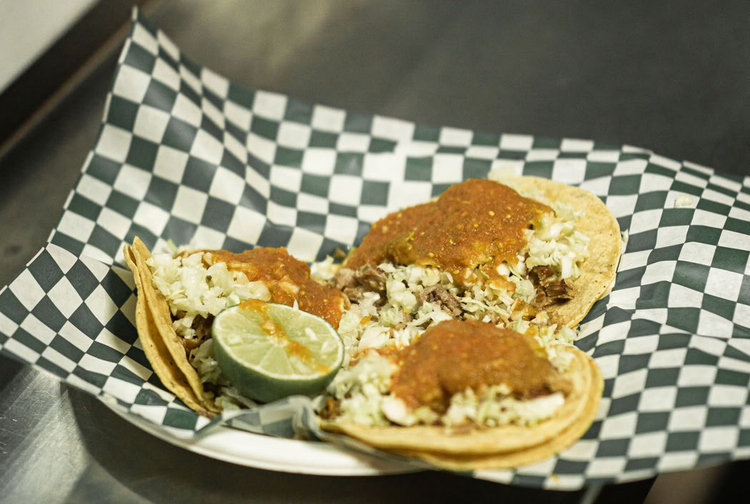 Three delicious tacos with toppings served on a checkered napkin in a restaurant setting.